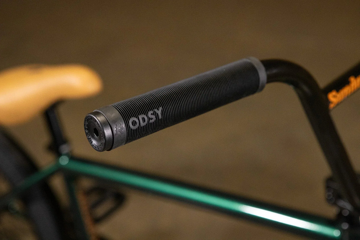 Gros plan d'une poignée de guidon BMX noire marque Odysy sur un cadre vert