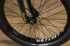 Gros plan d'une roue avant de BMX avec pneus Odyssey et fourche Sunday verte.