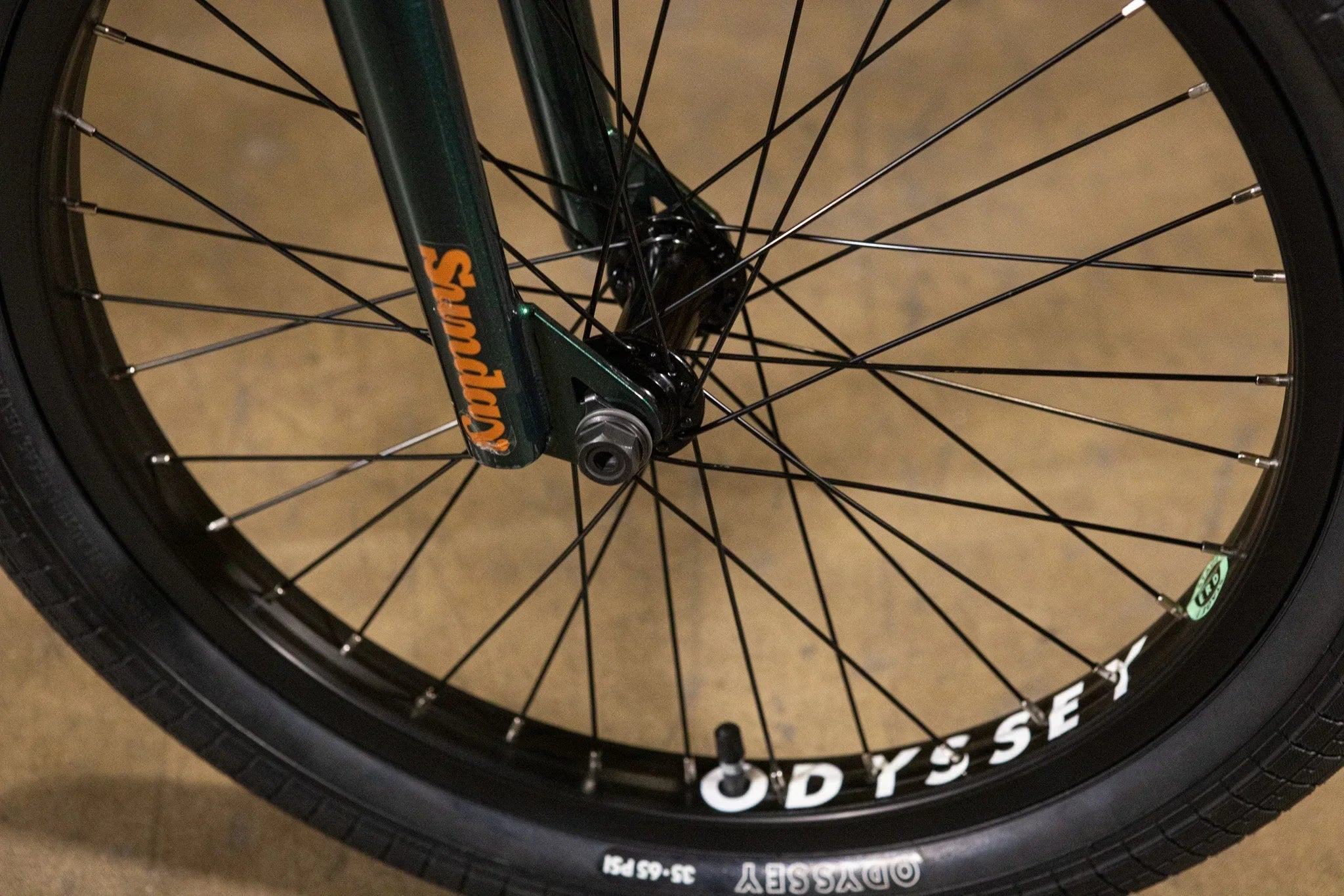 Gros plan d'une roue avant de BMX avec pneus Odyssey et fourche Sunday verte.