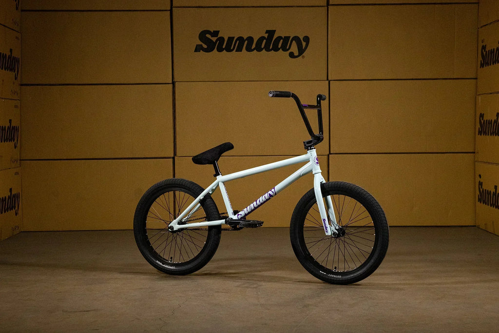 Vélo BMX blanc Sunday avec cadre blanc et pneus noirs sur fond de cartons.