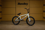 Vélo BMX blanc Sunday avec cadre blanc et pneus noirs sur fond de cartons.