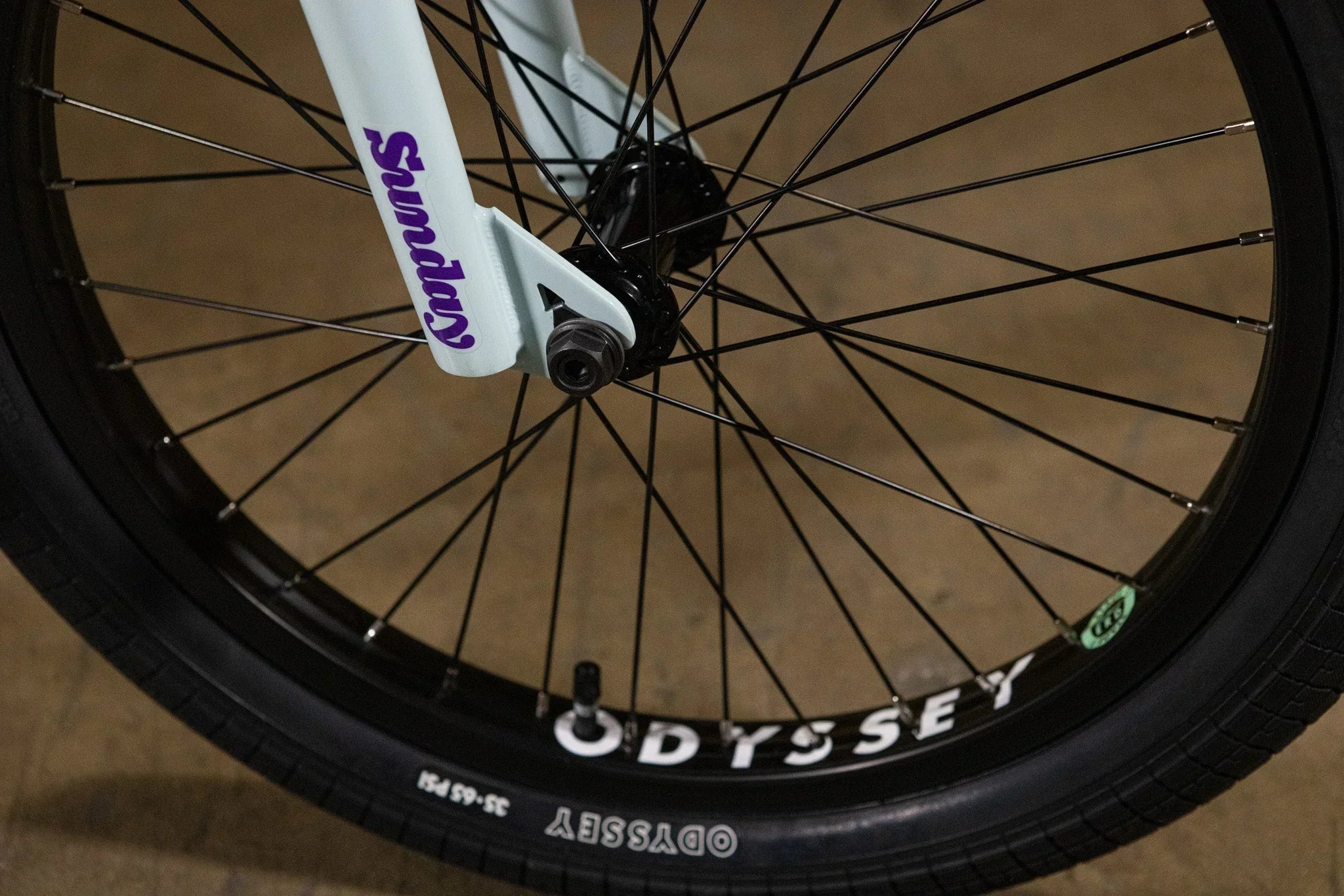 Gros plan d'une roue de vélo BMX avec pneus Odyssey et fourche Sunday blanche.