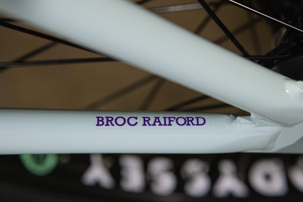 Gros plan du cadre blanc d'un vélo BMX avec l'inscription BROC RAIFORD en violet.