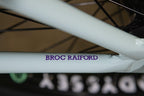 Gros plan du cadre blanc d'un vélo BMX avec l'inscription BROC RAIFORD en violet.