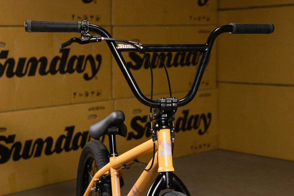 Gros plan du guidon et du cadre jaune d'un vélo BMX Sunday devant des cartons.