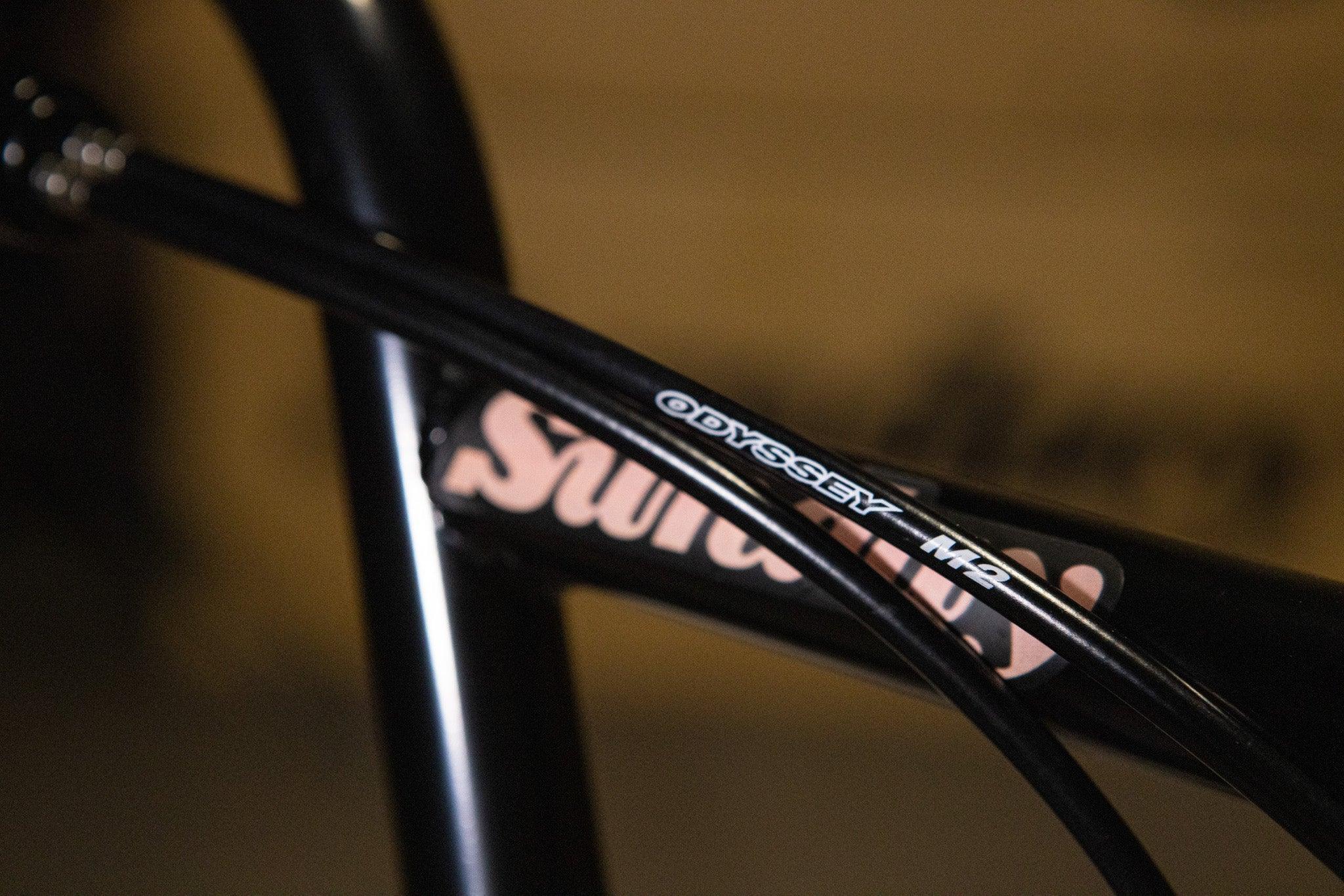 Gros plan d'un câble de frein Odyssey M2 sur un cadre de vélo BMX noir