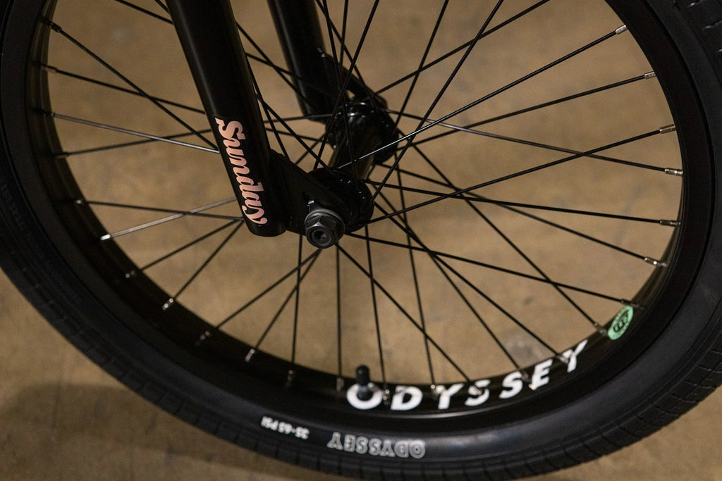 Gros plan d'une roue de vélo BMX avec pneu Odyssey et fourche Sunday noire.