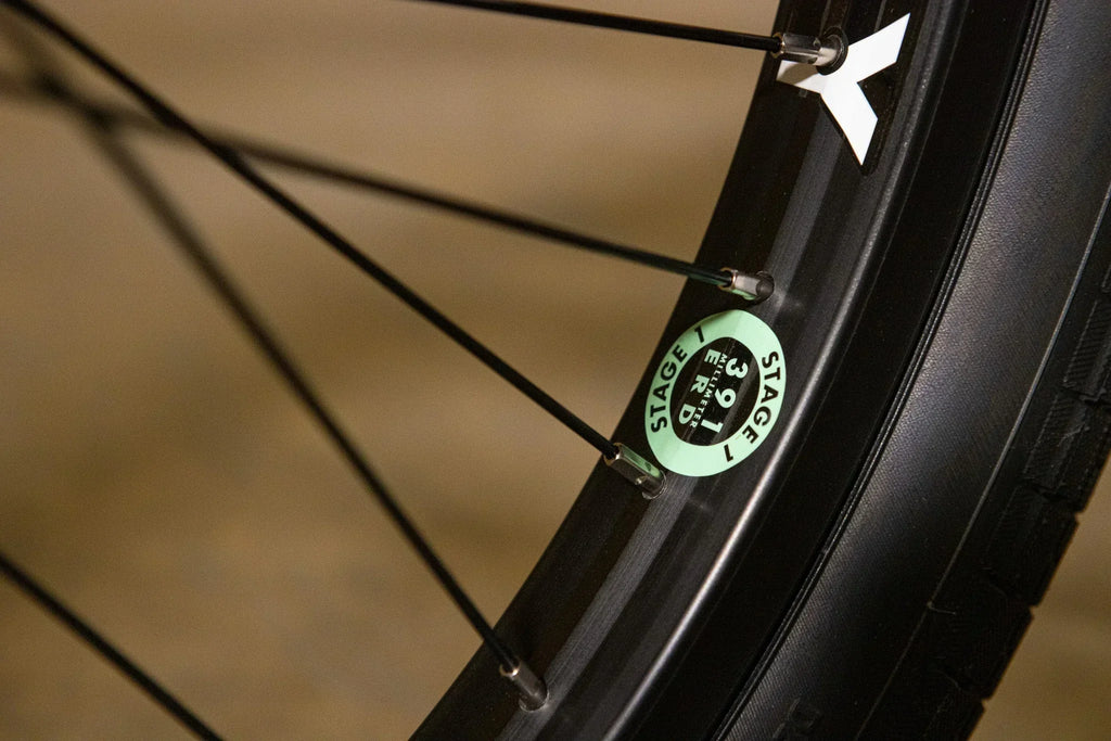 Détail d'une jante de vélo BMX avec rayons noirs et autocollant vert Stage 1 ERD