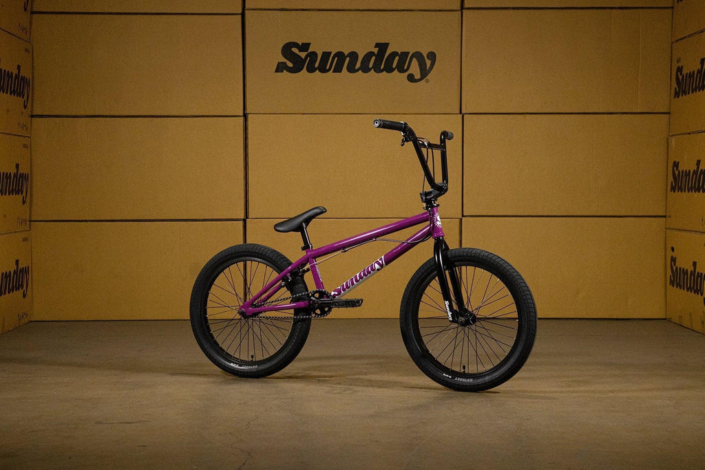 Vélo BMX Sunday violet sur fond de cartons beiges.