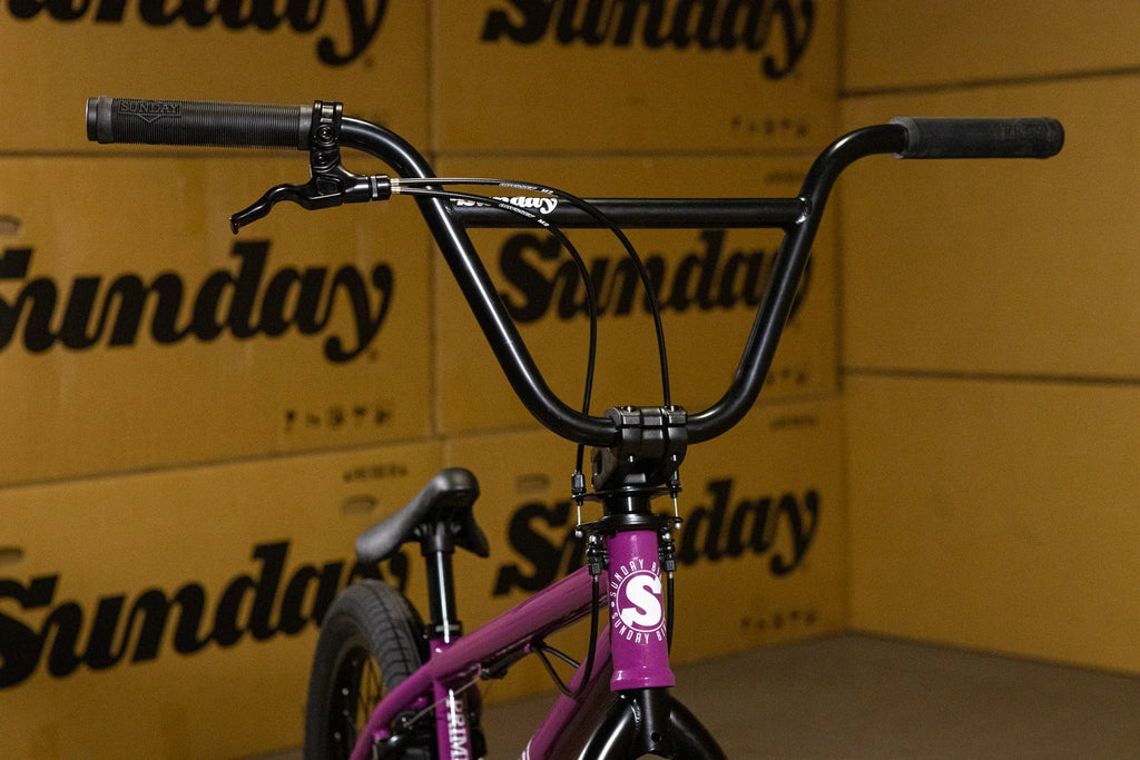 Gros plan du guidon noir et du cadre violet d'un vélo BMX Sunday