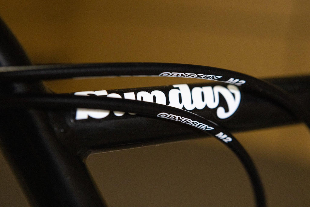 Gros plan des câbles de frein Odyssey M2 sur un cadre de vélo BMX Sunday noir.