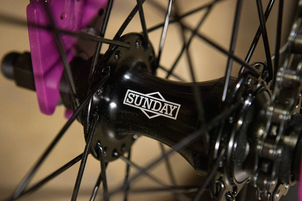 GHub de roue BMX Sunday noir avec rayons noirs et étrier de frein rose.