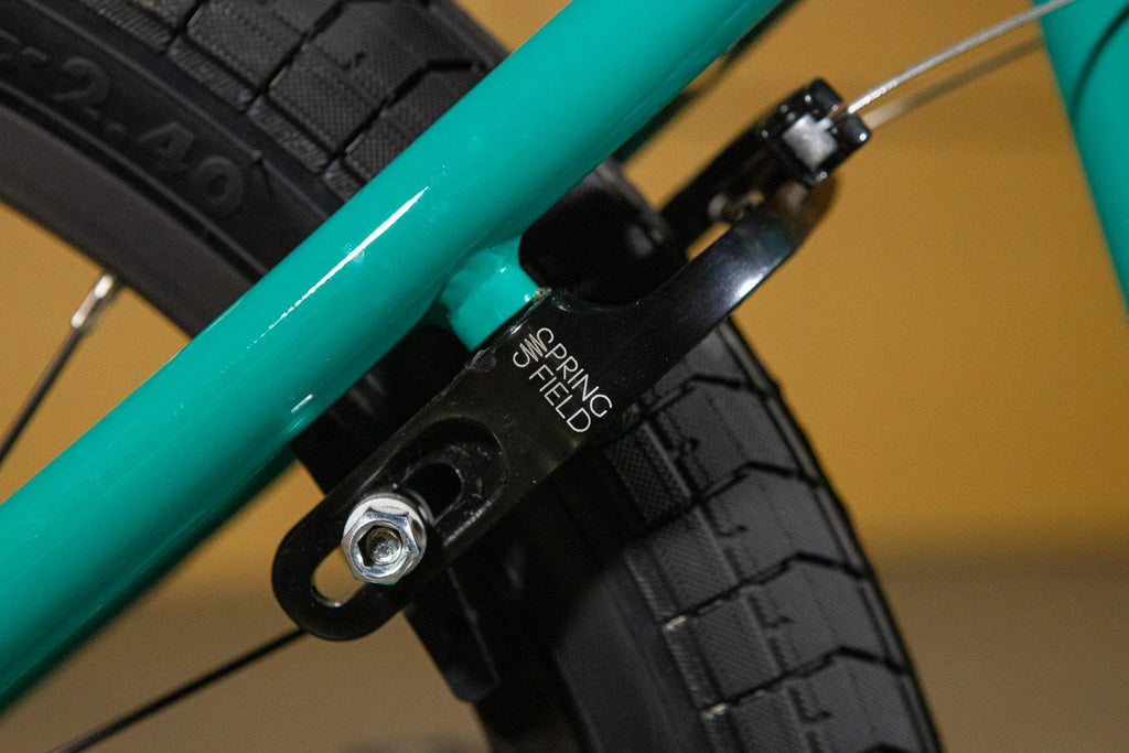 Détail d'un frein arrière noir Springfield sur un cadre de vélo BMX turquoise.