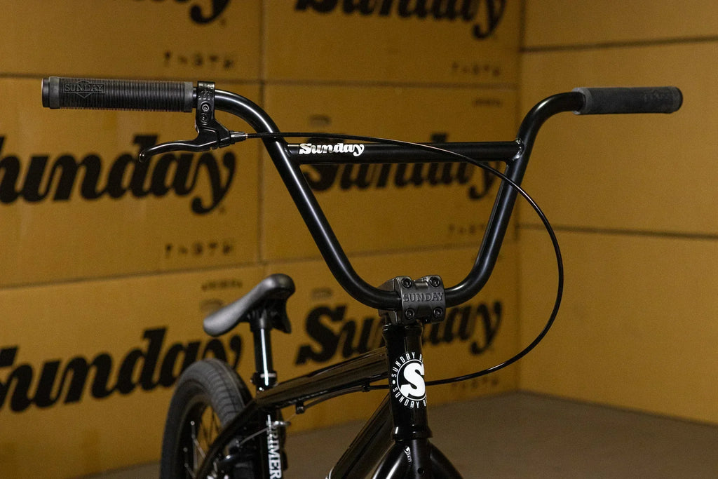 Gros plan du guidon noir d'un vélo BMX Sunday devant des cartons de marque.