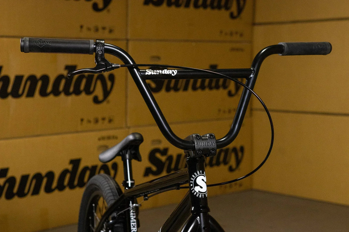 Gros plan du guidon noir d'un vélo BMX Sunday devant des cartons de marque.