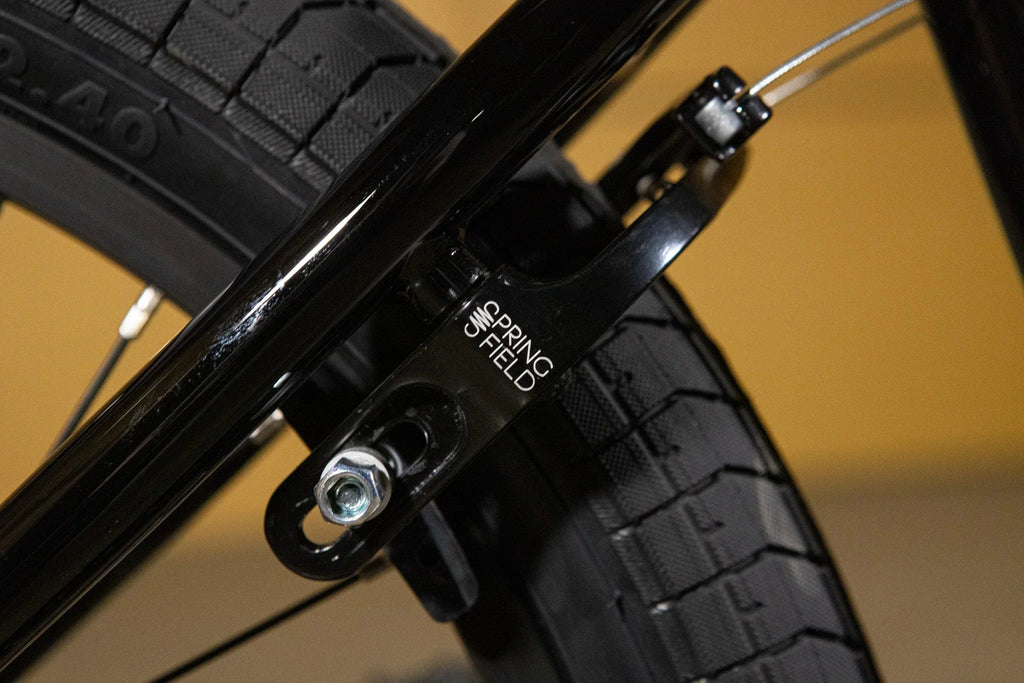 Détail d'un frein arrière Spring Field noir sur un pneu de vélo BMX.