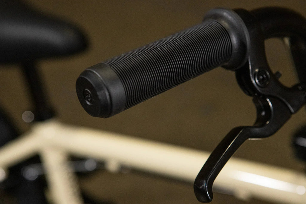 Gros plan d'une poignée et d'un levier de frein noirs sur un vélo BMX blanc.