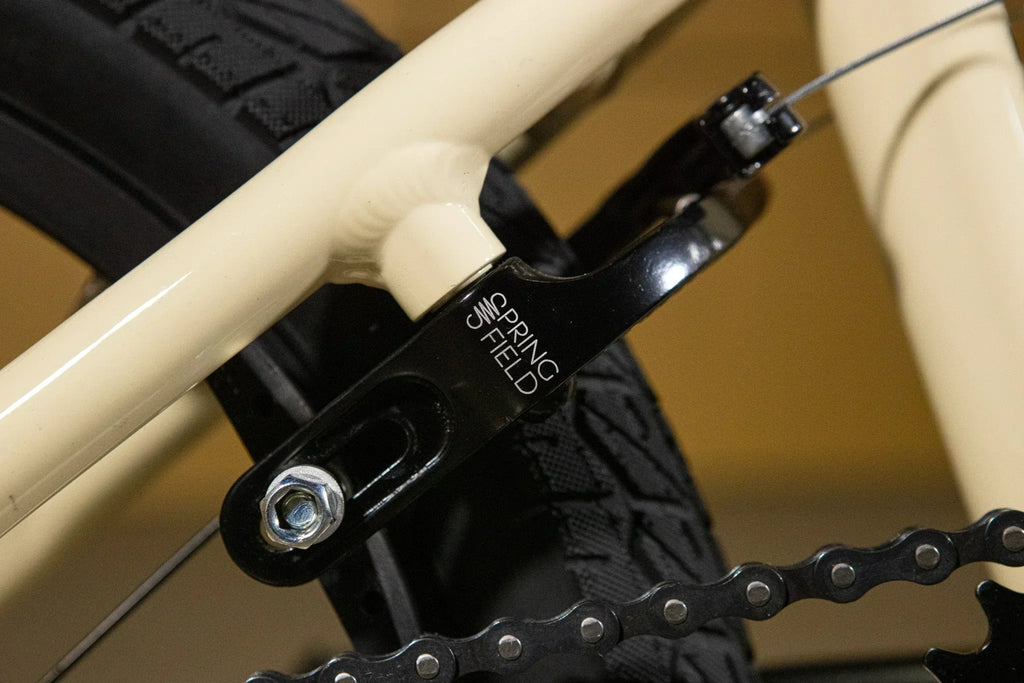 Gros plan d'un tendeur de chaîne Spring Field noir sur un cadre de vélo BMX crème.