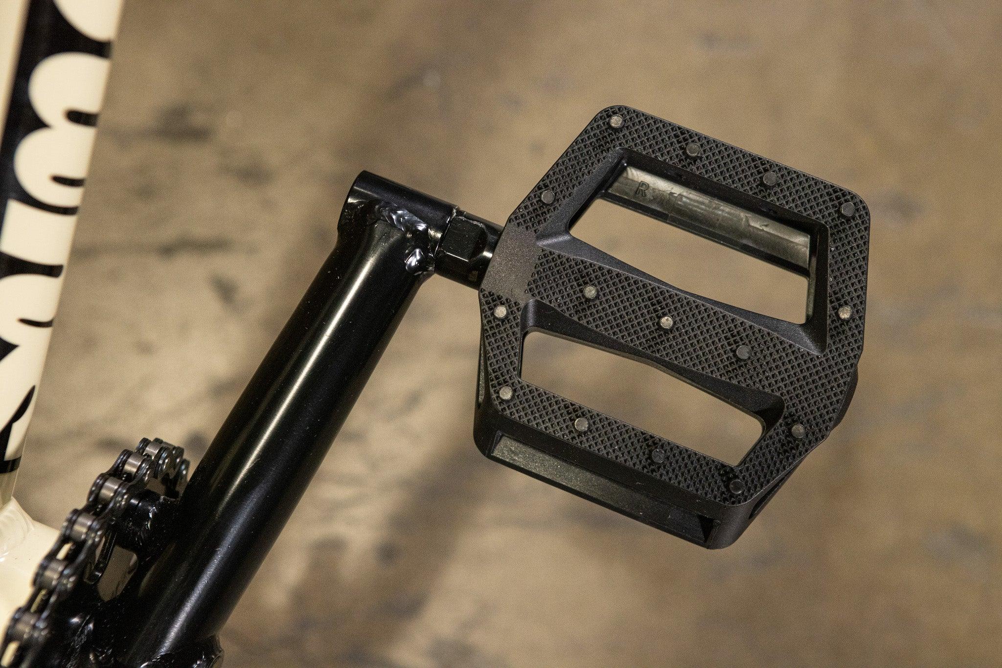 Gros plan d'une pédale plate noire pour vélo BMX avec picots antidérapants.
