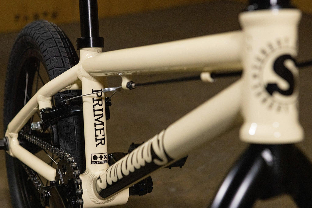 Gros plan du cadre beige d'un vélo BMX Primer avec pneus noirs.