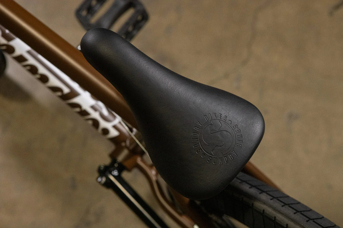 Gros plan d'une selle de vélo BMX noire avec logo embossé sur un cadre marron.