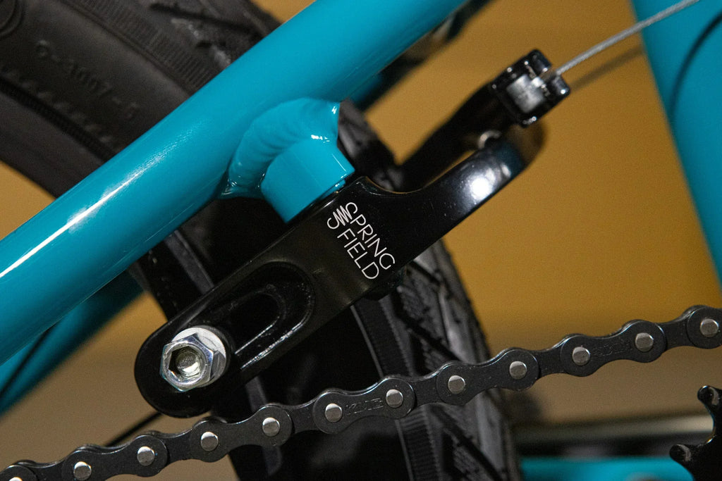 Détail d'un tendeur de chaîne Springfield noir sur un cadre de vélo BMX bleu turquoise.