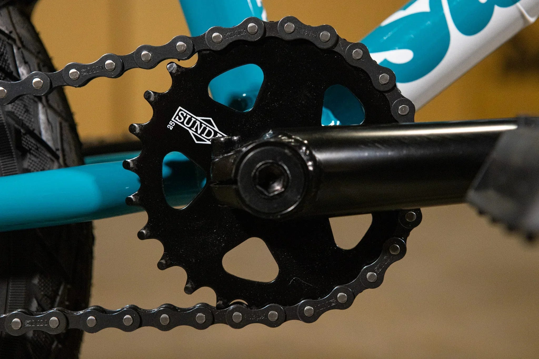 Gros plan d'un plateau de pédalier noir Sund sur un vélo BMX bleu.