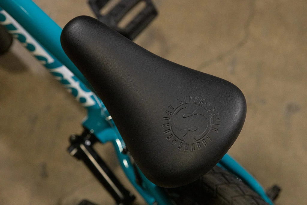 Gros plan d'une selle noire Sunday Bikes sur un cadre de vélo BMX bleu turquoise.