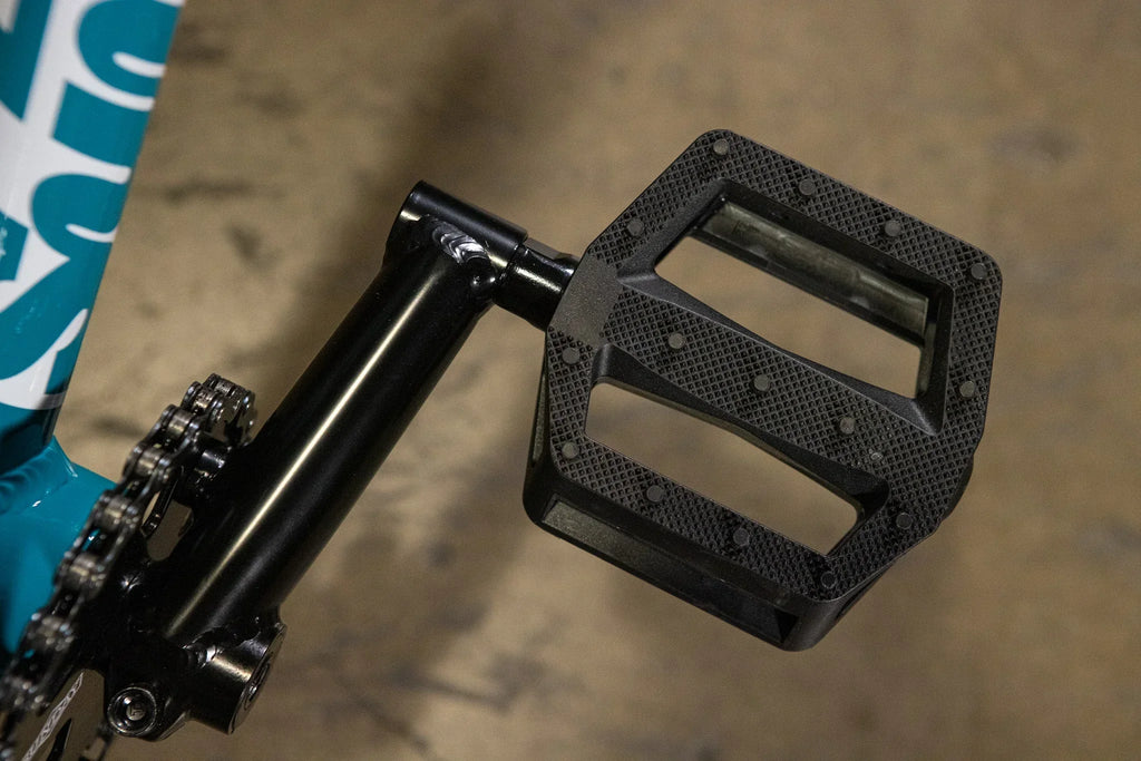 Gros plan d'une pédale plate en nylon noir avec picots antidérapants sur un vélo BMX.