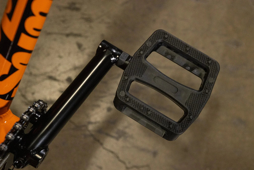 Gros plan d'une pédale plate en nylon noir montée sur un vélo BMX.