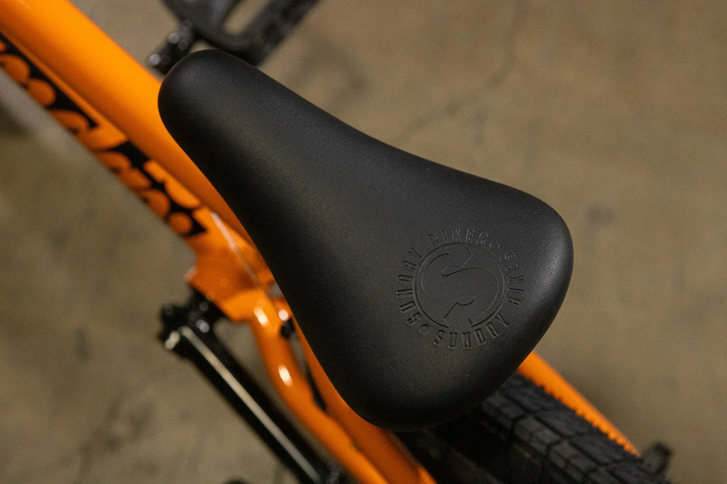 Gros plan d'une selle de vélo BMX noire sur un cadre orange vif.