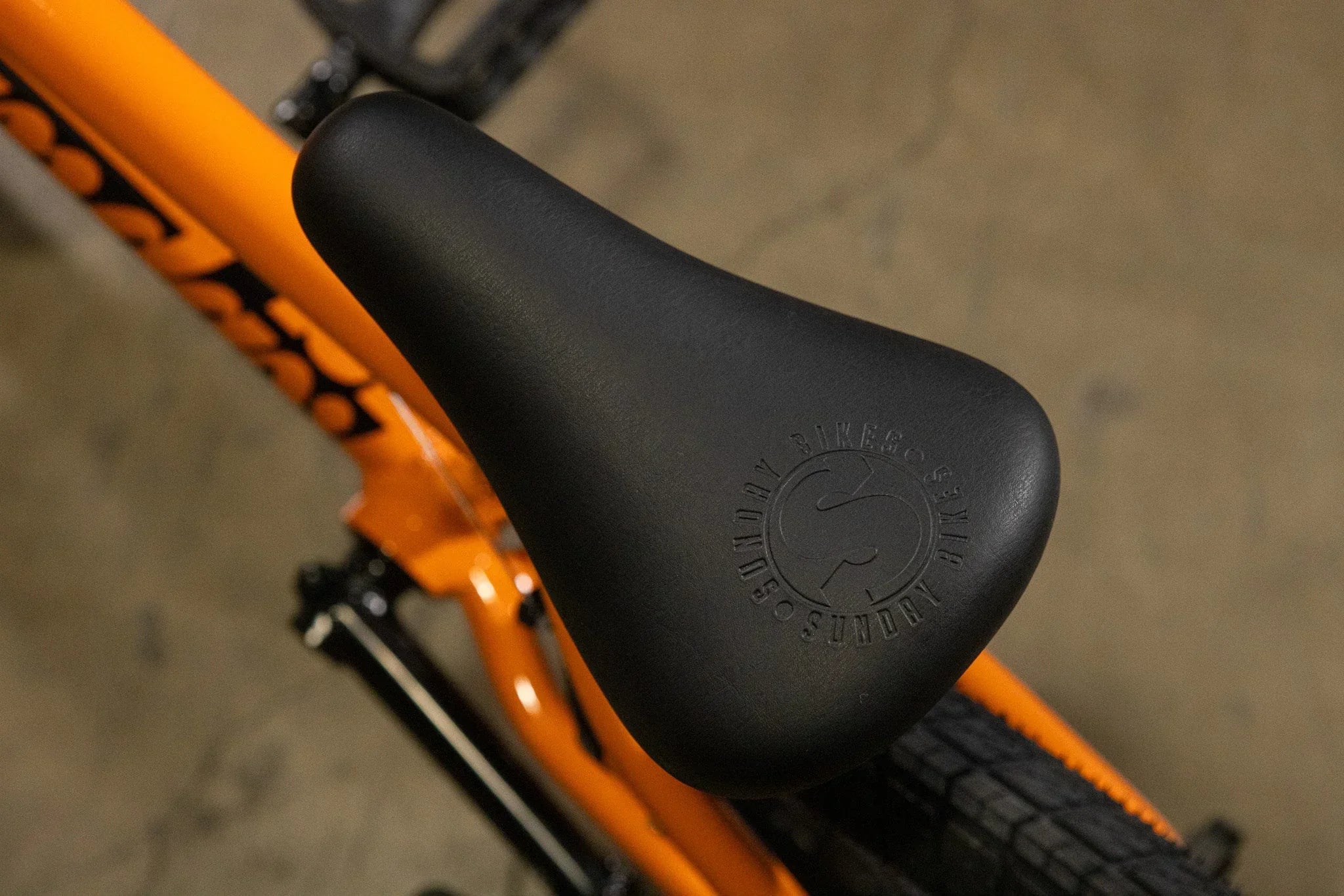 Gros plan d'une selle de vélo BMX noire sur un cadre orange vif.