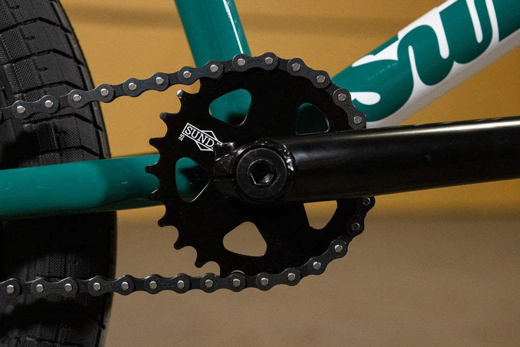 Gros plan d'un plateau Sund noir et d'une chaîne sur un cadre de vélo BMX vert.