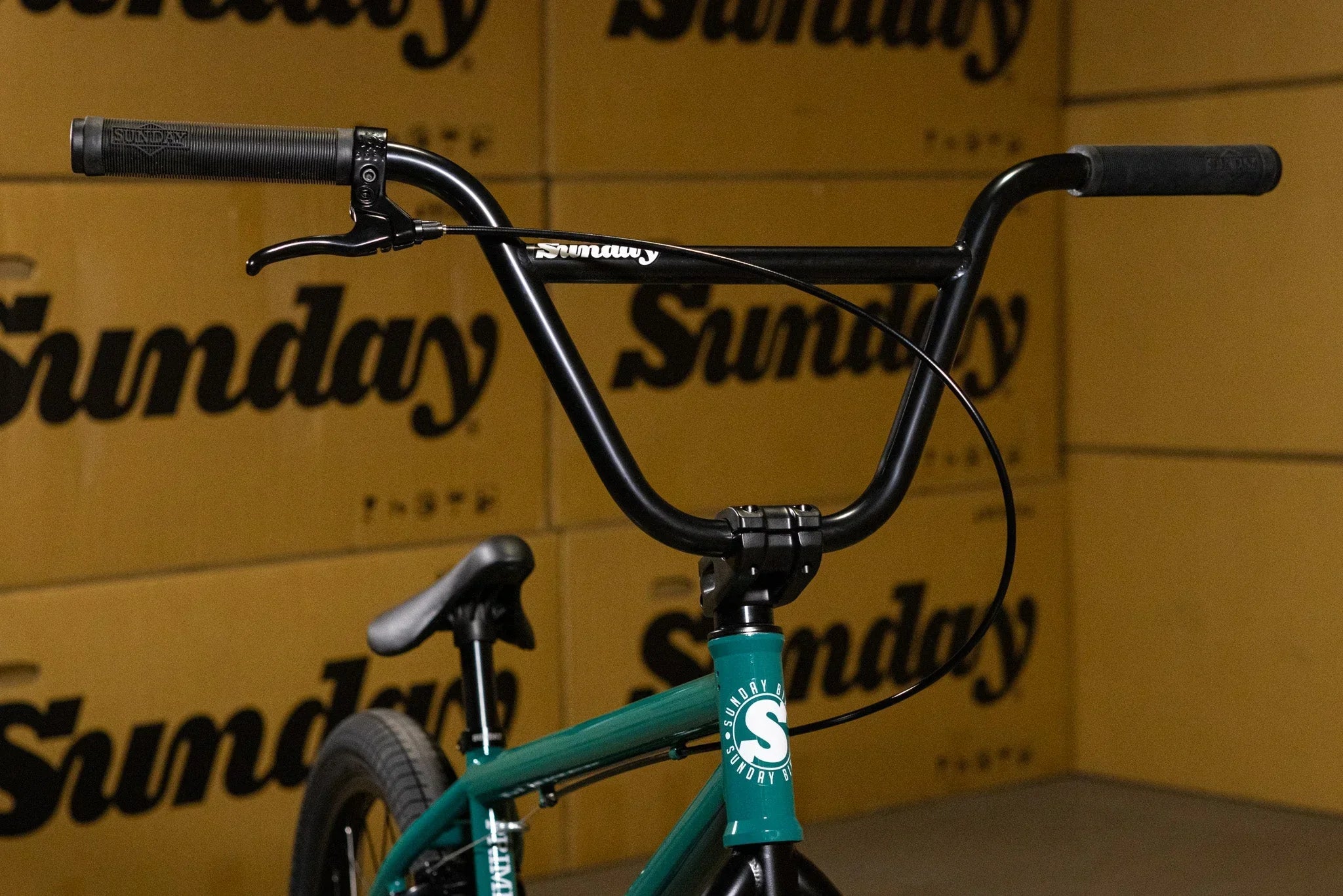 Gros plan du guidon noir et du cadre turquoise d'un vélo BMX Sunday devant des cartons.