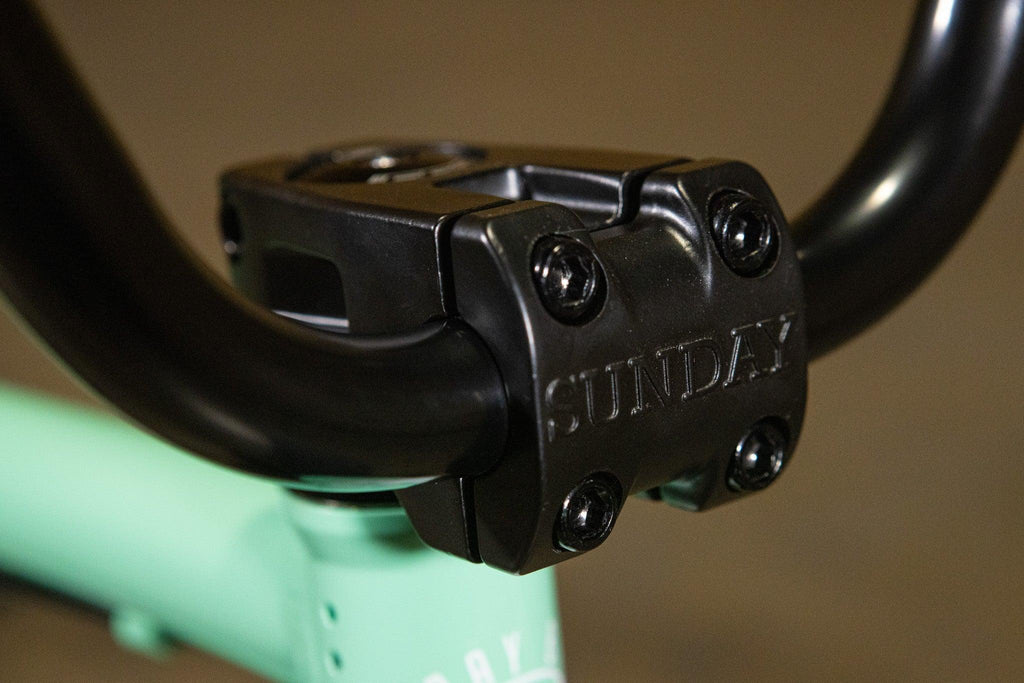 Gros plan d'une potence de vélo BMX noire de marque Sunday sur un cadre vert menthe.