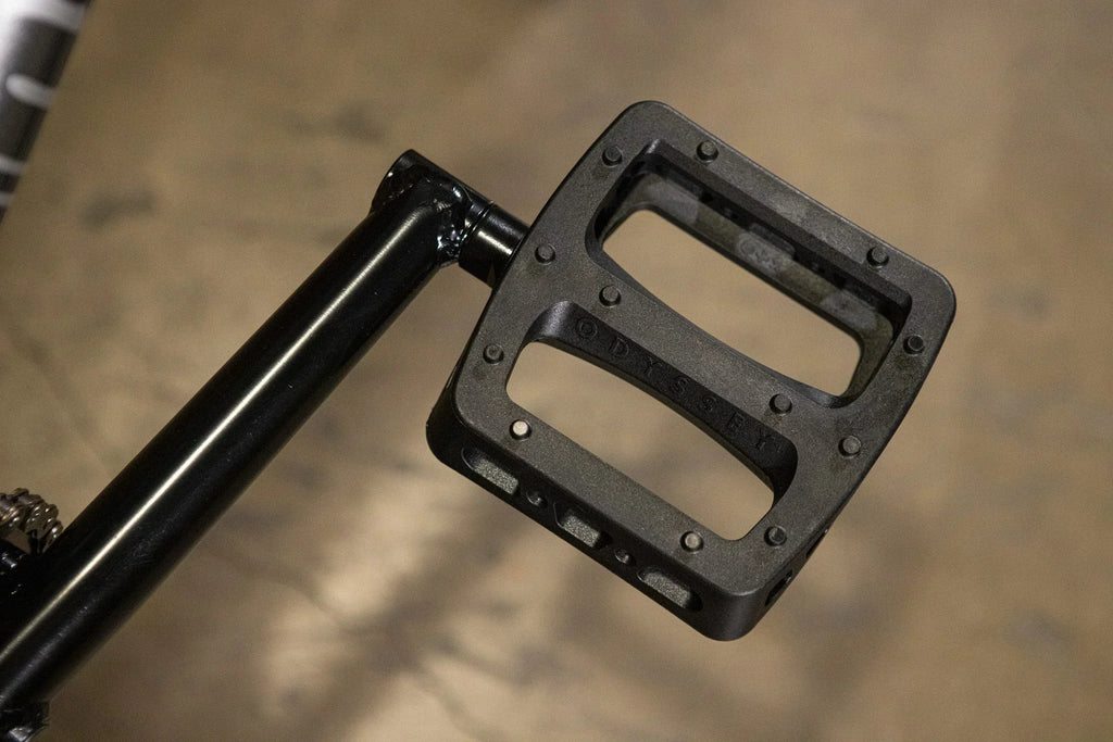 Gros plan d'une pédale plate Odyssey noire installée sur un vélo BMX.