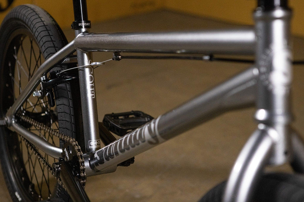 Détail du cadre argenté d'un vélo BMX avec pneus noirs