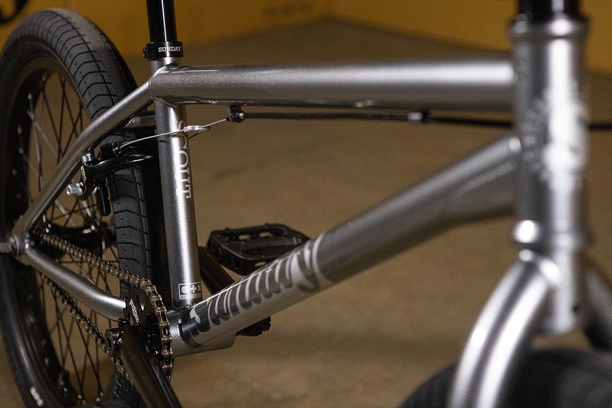 Détail du cadre argenté d'un vélo BMX avec pneus noirs
