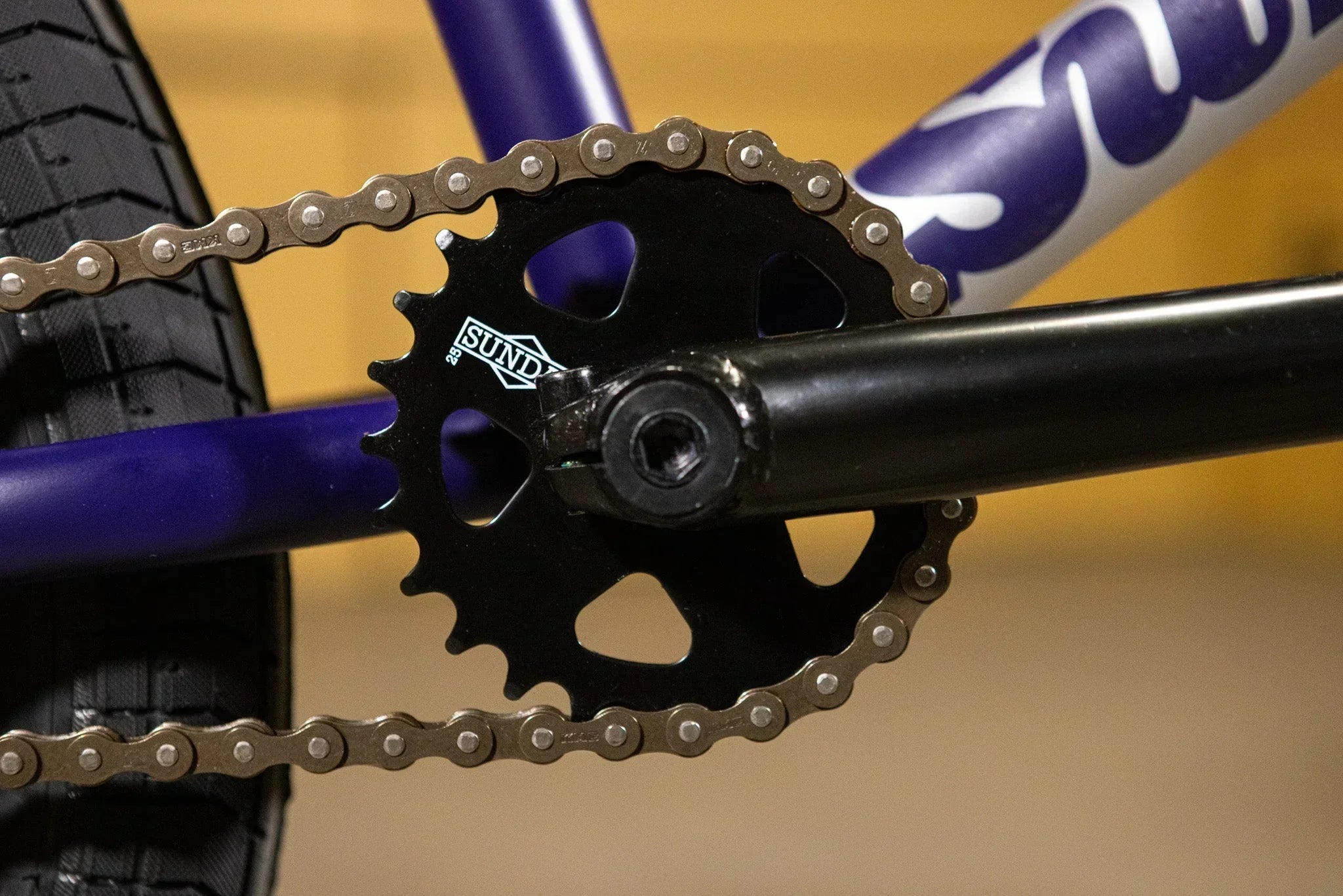 Gros plan du plateau Sund noir et de la chaîne sur un cadre de BMX violet