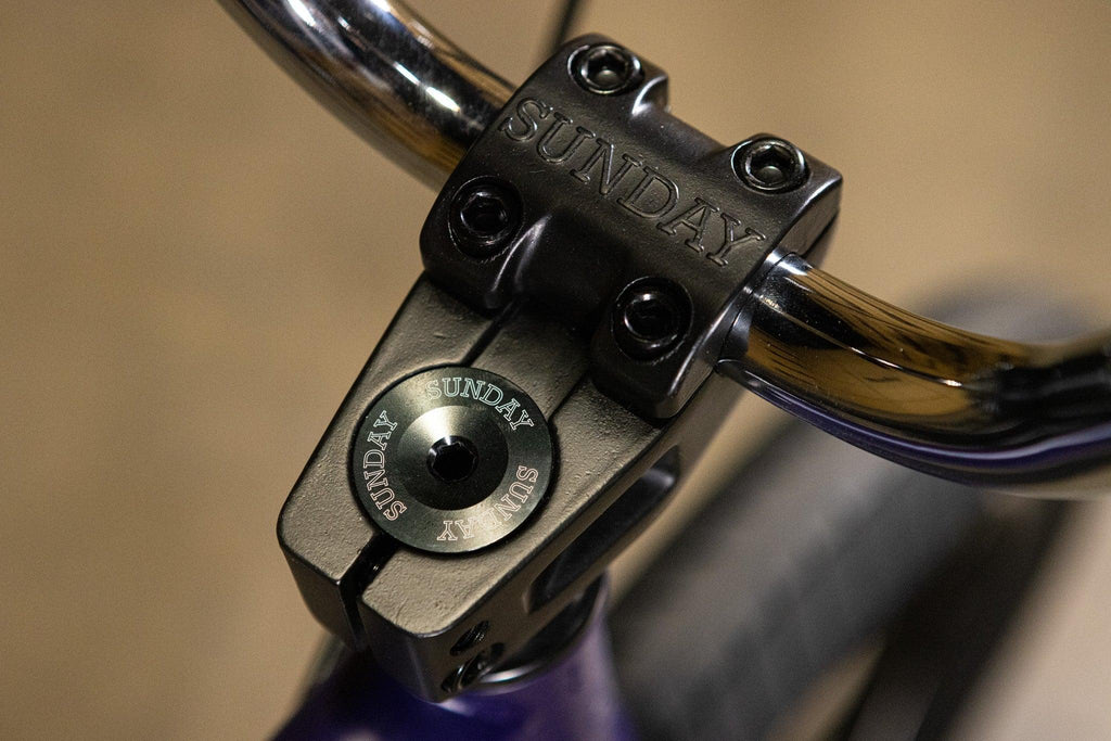 Gros plan d'une potence de vélo BMX noire marquée Sunday avec guidon chromé.