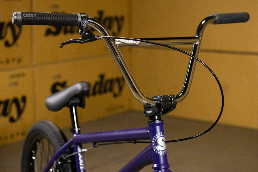 Gros plan du guidon chrome et du cadre violet d'un vélo BMX Sunday