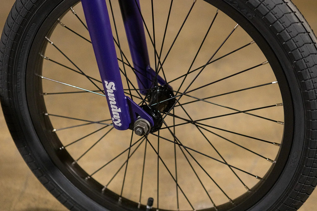 Gros plan sur la fourche avant violette et la roue d'un vélo BMX Sunday