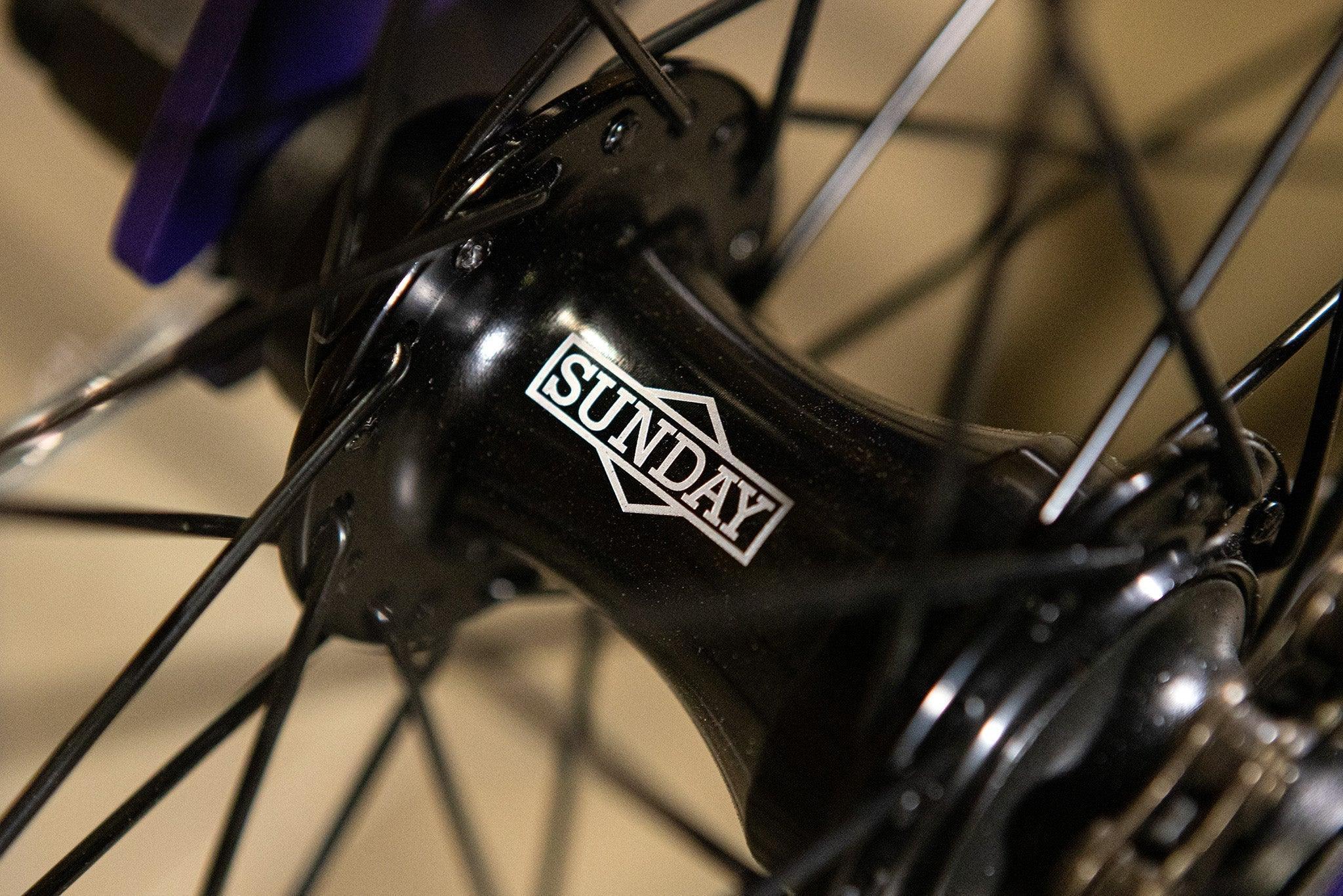 Gros plan d'un moyeu de roue BMX noir avec le logo Sunday blanc.