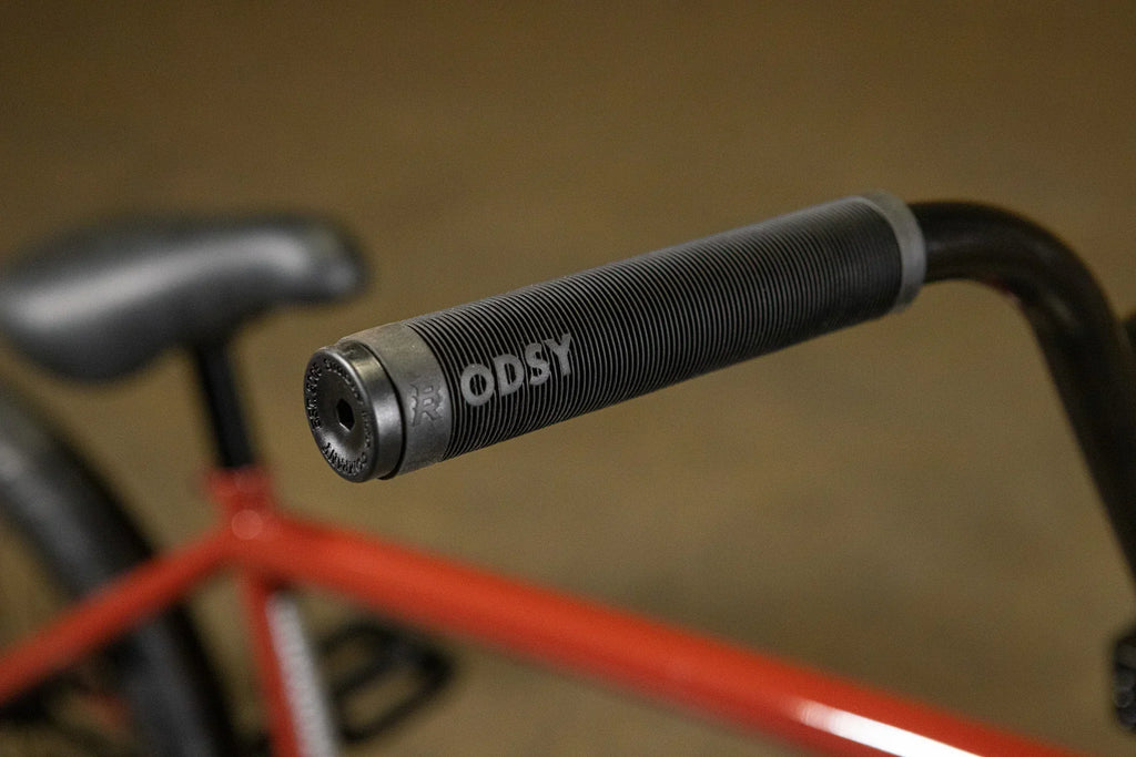 Gros plan d'une poignée de guidon BMX grise de marque Odyssey sur un vélo rouge.