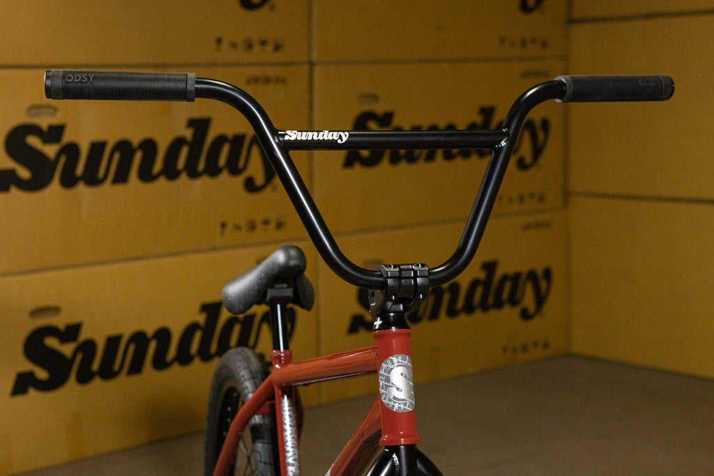 Guidon de vélo BMX Sunday noir sur cadre rouge devant des cartons Sunday