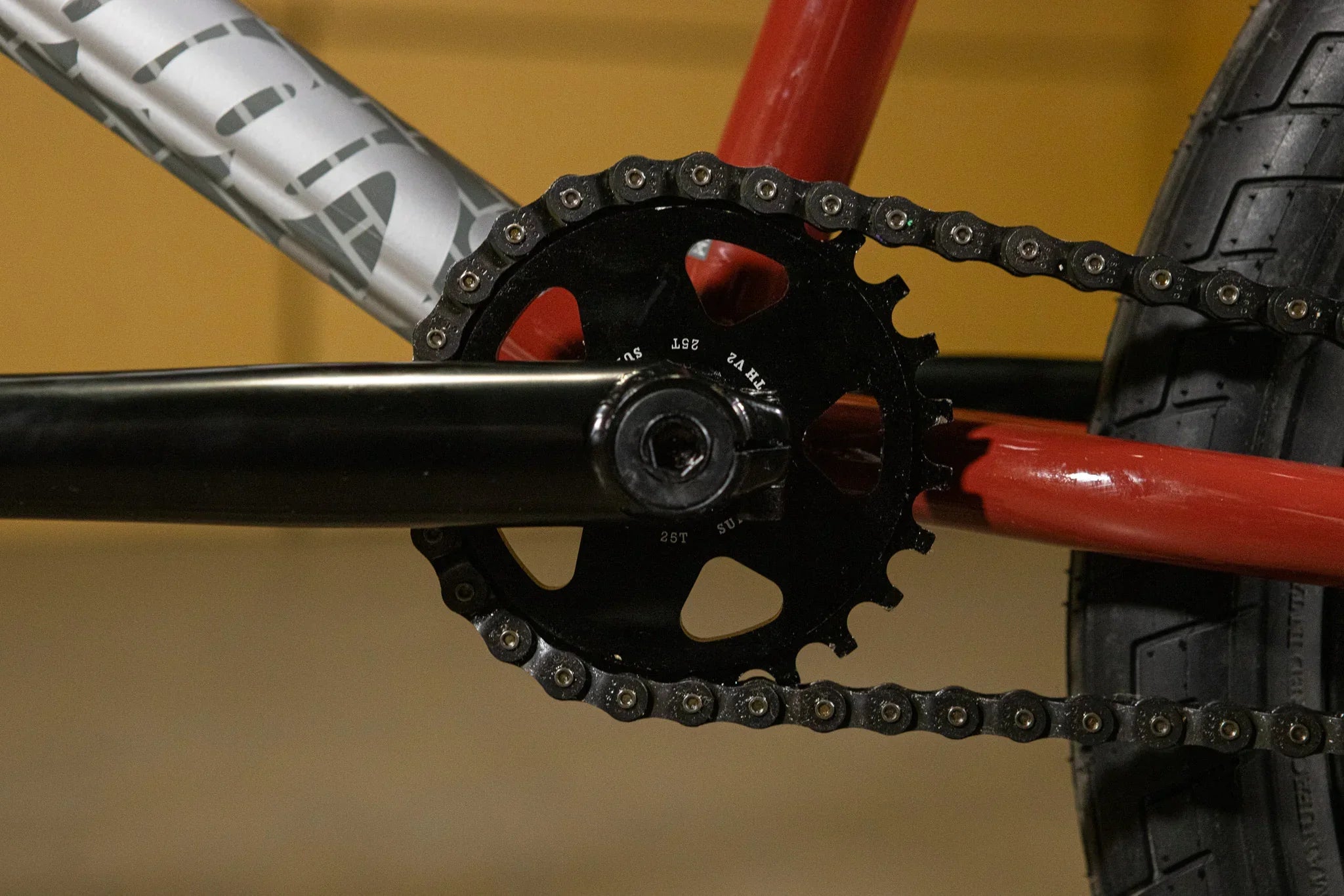 Gros plan d'un plateau et d'une chaîne de vélo BMX noir sur un cadre rouge.