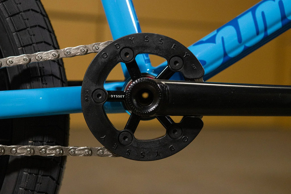 Gros plan d'un plateau de pédalier Odyssey noir sur un cadre de vélo BMX bleu