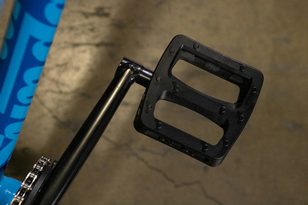 Gros plan d'une pédale de vélo BMX en nylon noir fixée à une manivelle noire.