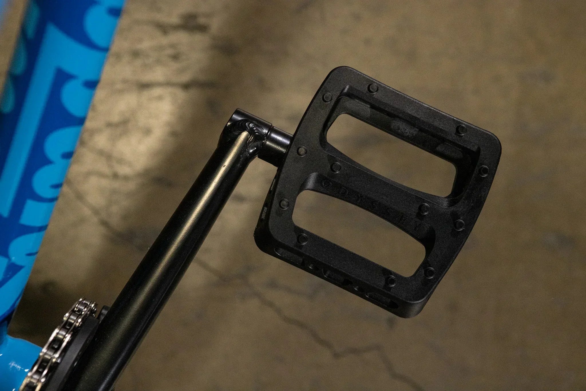 Gros plan d'une pédale de vélo BMX en nylon noir fixée à une manivelle noire.