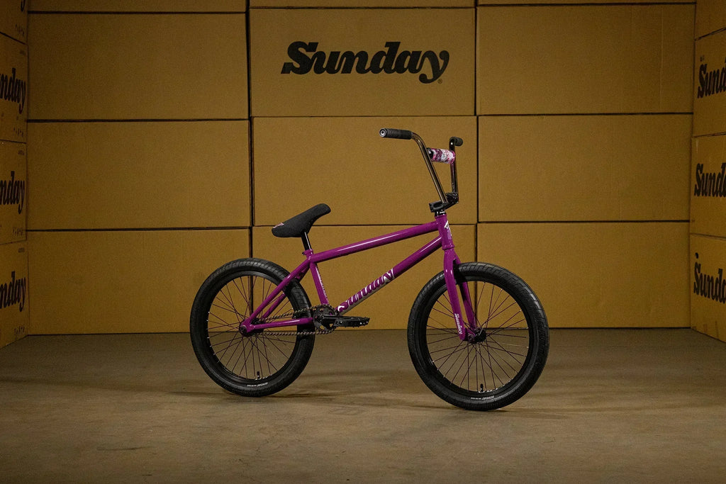 Vélo BMX Sunday violet avec cadre et fourche assortis devant des cartons de marque.